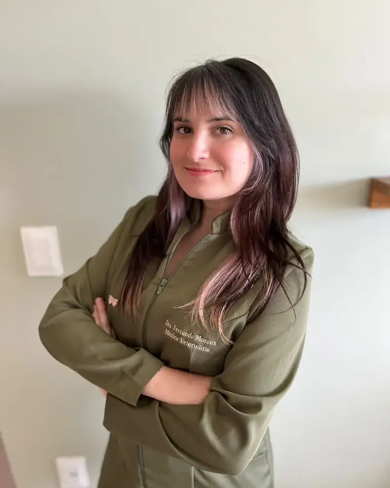 Dra. Fernanda Moraes, médica-veterinária, de jaleco, braços cruzados e sorrindo